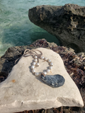 Pearl necklace with a shell pendant on a rock by the water