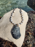 Pearl necklace with a shell pendant on a rock by the water