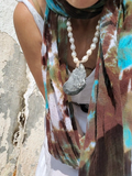 Person wearing a colorful scarf, pearl necklace, and white top against a stone wall.