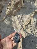 Hand holding a necklace with a large stone pendant against a stone wall background