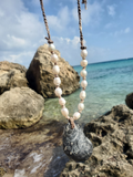 Necklace with shell and pearl beads hanging on a rock by the ocean