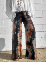 Tie-dye pants worn by a person against a white brick wall. The pattern is somewhat vertical