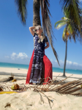 Woman in a dress standing on a beach with palm trees and blue sky.