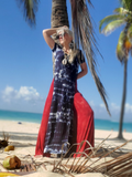 Woman in a tie-dye dress and red cover-up on a tropical beach with palm trees and blue sky.