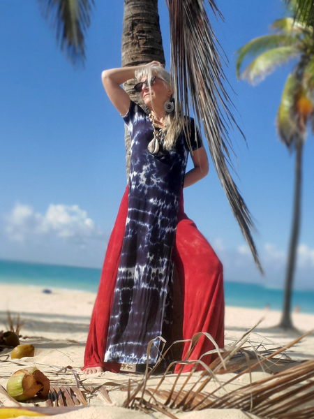 Woman in a tie-dye dress and red cover-up on a tropical beach with palm trees and blue sky.