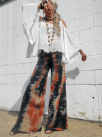 Person wearing a white blouse and tie-dye palazzo pants against a white wall.