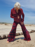 Person wearing a red jacket and tie-dye pants on a sandy beach.