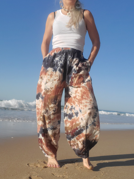 Person wearing tie-dye pants and a white tank top on a beach.