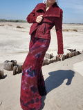Person wearing a red jacket and tie-dye pants standing on a sandy beach.