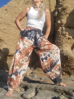 Person wearing tie-dye pants and a white top standing on a rocky beach. Patch pockets and side pockets