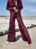 Person wearing a red jacket and tie-dye pants standing on a sandy beach.