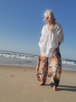 Person standing on a beach wearing a white top and patterned pants.