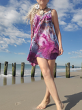 Person wearing a tie-dye dress on a beach with a blue sky and ocean in the background