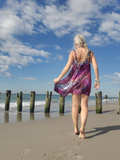 Woman in a purple dress walking on a beach with wooden posts and ocean in the background