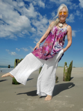 Woman in colorful top and white pants on a beach with blue sky and clouds.
