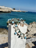 Jewelry with turquoise and pearl beads on a wooden post by the ocean.