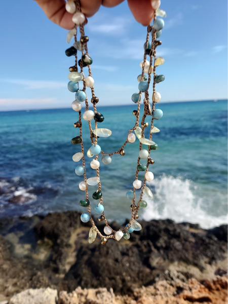 crocheted beaded necklace held in layers with the sea behind