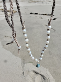 Necklace with white pearl beads and a blue larimar pendant on a sandy background
