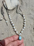 Pearl necklace with a blue stone pendant on sand