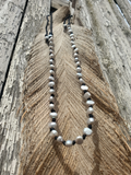 Necklace knotted on a black hemp with silver pearl beads on a wooden surface