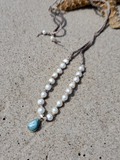 Pearl necklace with a blue larimar pendant on a sandy beach