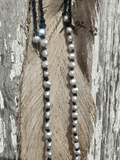 Pearl necklace with black cord draped over a textured surface