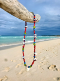 Colorful beaded necklace with shell elements on a beach with ocean and sky in the background