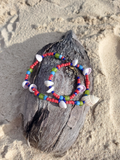 Colorful beaded bracelet on a piece of driftwood with sand in the background