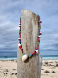 Colorful beaded necklace with shells on a wooden post by the beach