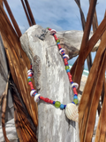 Colorful beaded bracelet with a shell on a piece of driftwood.