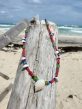 Colorful beaded necklace with shells on a piece of driftwood by the beach.