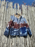Tie-dye jacket on a wooden surface with a wooden fence and blue sky in the background