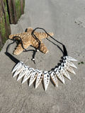 A handmade statement necklace made of ten white sliced shells attached to a black braided cord, displayed on a sandy beach next to a starfish prop.