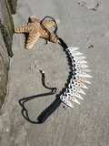 A handmade necklace made of multiple white seashell points attached to a black braided cord, displayed on a sandy beach next to a starfish.