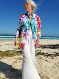Person wearing a colorful tie-dye shirt and white pants on a beach.