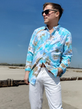 Man wearing a blue tie-dye shirt and sunglasses on a beach.