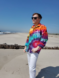 Person wearing a colorful tie-dye shirt and sunglasses on a beach.