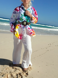 Person wearing a colorful shirt and white pants standing on a beach with blue sky and ocean.
