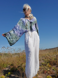 Person in a field wearing a colorful top and white pants with a clear blue sky.