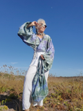 Person wearing a colorful kimono-style garment in a natural setting with a clear blue sky.
