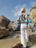 Person wearing a colorful kimono-style garment on a beach with rocky cliffs.