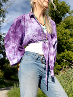 Person wearing a purple tie-dye shirt outdoors with trees in the background