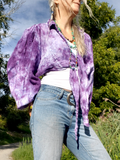 Person wearing a purple tie-dye shirt outdoors with trees in the background