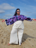 Person wearing a colorful top and white pants on a sandy beach with blue sky.