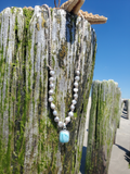 silver pearls adjustable necklace with a blue pendant hanging  with a starfish on a piece of wood