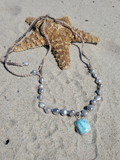 silver pearls adjustable necklace with a blue pendant laying on the sand with a starfish