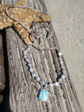 silver pearls adjustable necklace with a blue pendant laying on  an old drift wood with a starfish