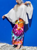 A fun and bright photo; I took this selfie front of a royla blue wall; I'm modeling a tie dye rainbow galaxy maxi skirt with fold over waistband, barefooted, with a white flowy boho cold shoulder top and shell jewelry.