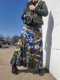 Person wearing a tie-dye skirt and leather jacket against a white wall.