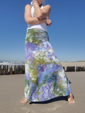 Woman wearing a colorful skirt on a beach with a clear blue sky.